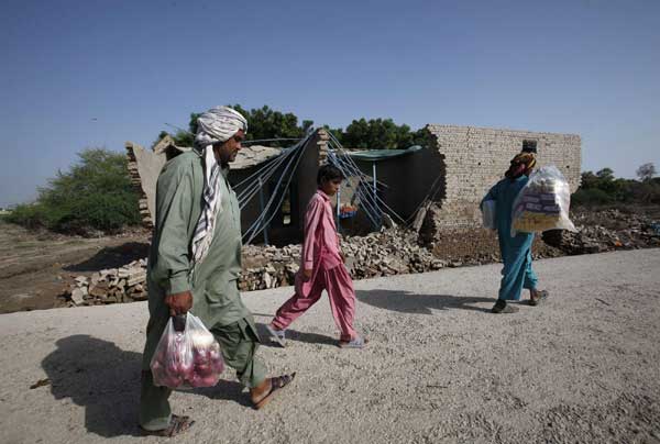 Villagers, displaced by flooding, carry their supplies as they walk past a damaged house while returning to their flooded village in Dadu. [China Daily/Agencies]