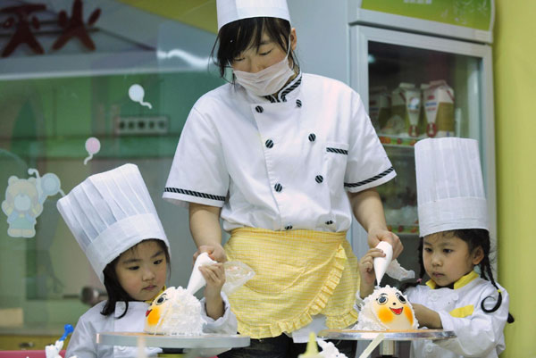 Girls are helped by an instructor as they decorate a cake during a cooking class at a youth recreation centre in Shenyang, Liaoning province on Friday. [China Daily/Agencies] 