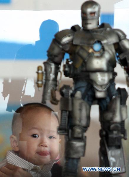 A child is seen with a model of a Hollywood movie character the Iron Man produced by a local studio at a comic and animation exhibition in Dongguan, south China&apos;s Guangdong Province, Oct. 3, 2010.[Chen Fan/Xinhua]