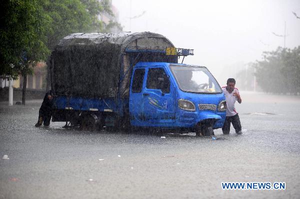 People struggle to move a switched-off vehicle on a waterlogged street in Qionghai, south China's Hainan Province, Oct. 5, 2010. [Xinhua/Meng Zhongde]