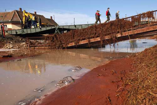 Locals cross a pontoon bridge next to a broken bridge in the flooded village of Kolontar, 150 km (93 miles) west of Budapest Oct 7, 2010. [China Daily/Agencies]