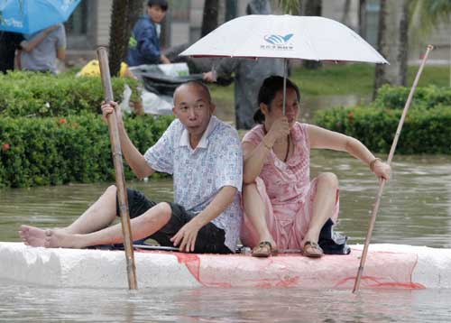Resident Li Xiong (left) and his wife use a piece of plastic boarding and bamboo poles on Thursday to navigate their way in Qionghai, Hainan province, which has been hit by continuous rain for a week. [China Daily]