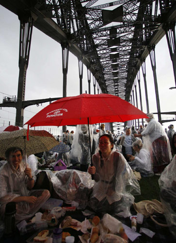 People picnic and have breakfast on the main deck of the Sydney Harbour Bridge as it rains during the Breakfast on the Bridge event in central Sydney Oct 10, 2010. [China Daily/Agencies]