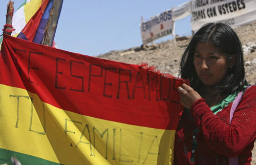 Veronica Quispe, wife of Bolivian miner Carlos Mamani who is among the 33 miners trapped underground in the San Jose Mine, holds her national flag with the words, &apos;Your family is waiting for you,&apos; as she stands on a hill above the area where the rescue operation continued in Copiapo Oct 11, 2010. [China Daily/Agencies]