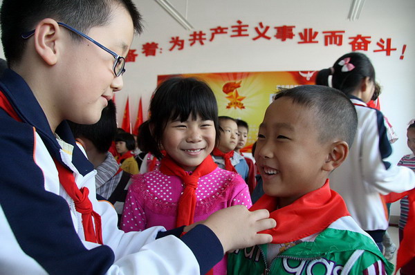 A league member (left) ties a red scarf for a new member in the 61st anniversary celebration ceremony held by a school in Weihai, Shandong province, Oct 12, 2010. [Xinhua]