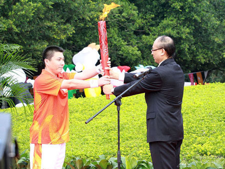 The first torchbearer Liu Gang (L) receives 'The Tide' at the Torch Relay for the 16th Asian Games in Shenzhen.