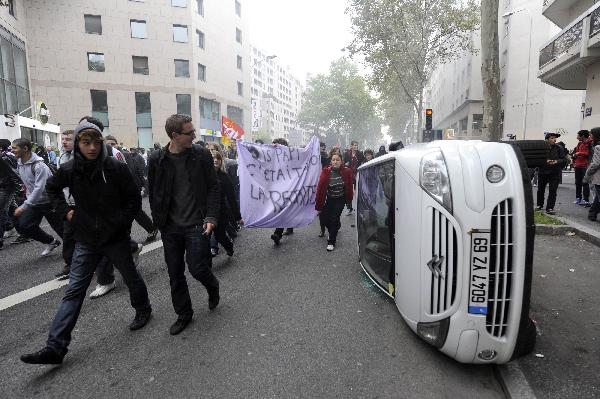 Students overturn a car during a demonstration over pension reforms with private and public sector workers in Lyon October 18, 2010. [Xinhua]