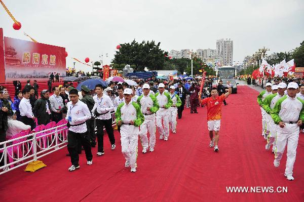 The first torchbearer Sun Shuwei (C) holds the torch aloft during the torch relay for the 16th Asian Games in Jieyang City, south China&apos;s Guangdong Province, Oct. 23, 2010. [Xinhua] 
