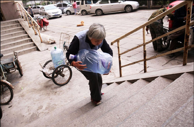 Gao Meiyun, 70, delivers water to customer at Yang village of Shijingshan district on Ocotber 19, 2010 in Beijing, China. Gao, weight 37.5kg, for supporting her disabled son and retarded grandson has to deliver 40 - 60 containers water which per one weight 20kg every day. Gao left hospital just few days due to her pleurisy and shock. Since then volunteets help the older woman deliver water every Wednesday afternoon. [sohu.com]