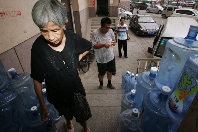 Gao Meiyun, 70, stocks from water works at Yang village of Shijingshan district on July 29, 2010 in Beijing, China. Gao, weight 37.5kg, for supporting her disabled son and retarded grandson has to deliver 40 - 60 containers water which per one weight 20kg every day. [sohu.com]