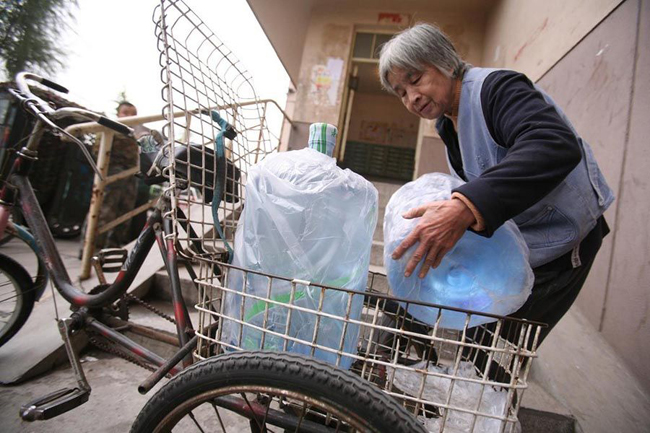 Gao Meiyun, 70, puts on water for delivering at Yang village of Shijingshan district on Ocotber 19, 2010 in Beijing, China. Gao, weight 37.5kg, for supporting her disabled son and retarded grandson has to deliver 40 - 60 containers water which per one weight 20kg every day. [sohu.com]