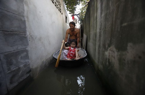 A man pushes his daughters on makeshift float as he wades through floodwaters in a narrow alleyway in Bangkok October 25, 2010. Floodwaters from northeast provinces, which have swamped thousands of acres of farmland, have spread to the Thai capital.[China Daily/Agencies] 