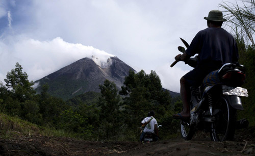 Villagers ride on motorcycles as Mount Merapi volcano emits smoke from Cangkringan village October 25, 2010. [China Daily/Agencies] 