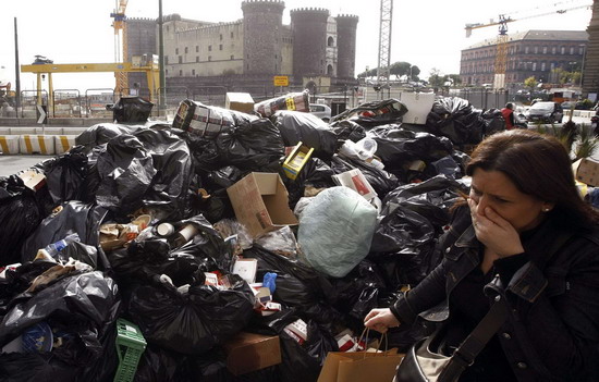 A woman on a sidewalk covers her mouth near a pile of garbage in downtown Naples Oct 22, 2010. Italian Prime Minister Silvio Berlusconi pledged a swift end to the Naples garbage crisis on Friday as TV pictures of piles of rubbish and angry protests put his struggling government under pressure.[China Daily/Agencies]