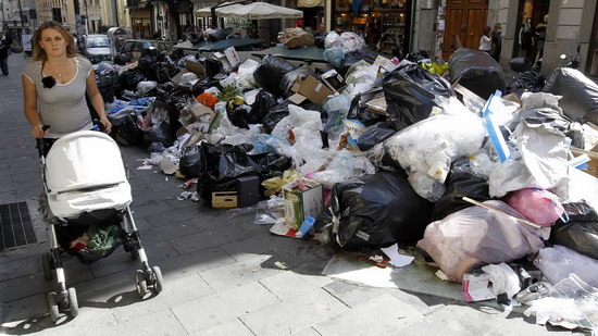 A woman pushes a stroller near a pile of garbage in downtown Naples Oct 22, 2010. [China Daily/Agencies]