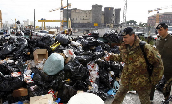An army officer walks past a pile of garbage in downtown Naples Oct 22, 2010. [China Daily/Agencies]