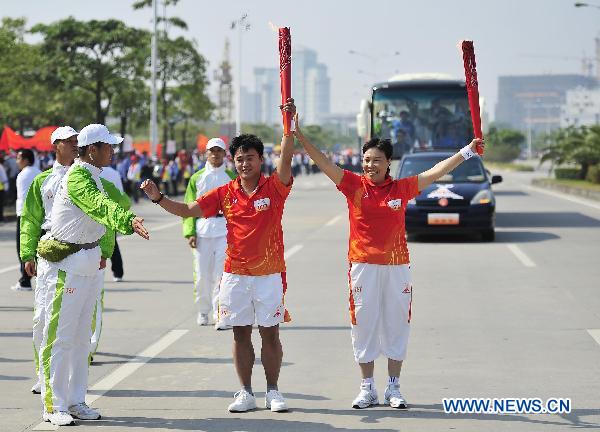 The 77th torchbearer Hu Jia (L) and the 76th torchbearer Mai Nangui hold the torch aloft during the torch relay for the 16th Asian Games in Zhanjiang City, south China's Guangdong Province, Nov. 1, 2010. (Xinhua/Liang Xu)