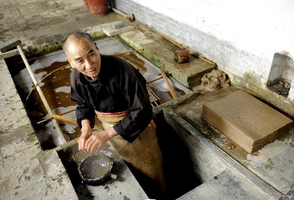 Ma Lingzhong warms hands in hot water when processing papermaking materials in Longting Town, northwest China's Shaanxi Province, on Oct. 27, 2010. The 73-year-old Ma Lingzhong and 60-year-old Wang Qingxia were two of the few who could make paper in the way Cai Lun, the inventor of paper, did 1,900 years ago. They were invited to show the papermaking process at Cai Lun Paper Culture Museum in Longting Town. [Xinhua photo] 