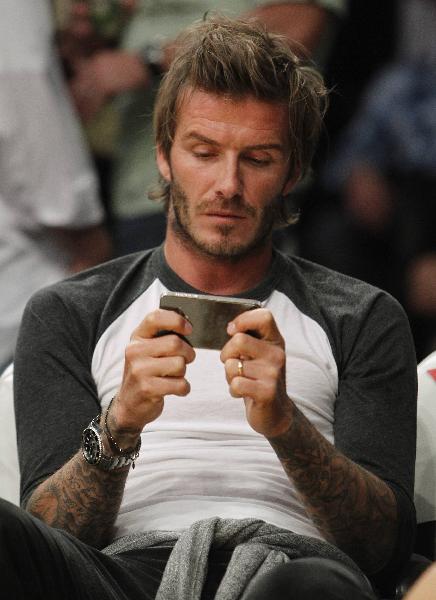 Soccer player David Beckham uses an Apple iPhone mobile phone as he attends the NBA basketball game between the Los Angeles Lakers and the Memphis Grizzlies in Los Angeles November 2, 2010. (Xinhua/Reuters Photo)