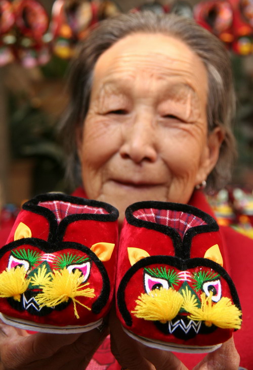 An elderly shows displays tiger-like shoes made by hand in time for winter in Tancheng town, Linyi city of China&apos;s east Shandong province on Nov 7, 2010. [Xinhua]