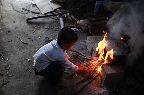 Along makes a fire to prepare for dinner. His grandmother, who lives 15 minutes’ walk away, built two vegetable plots for him, and pays regular visits despite not living with him. Photo taken on Nov 2, 2010.