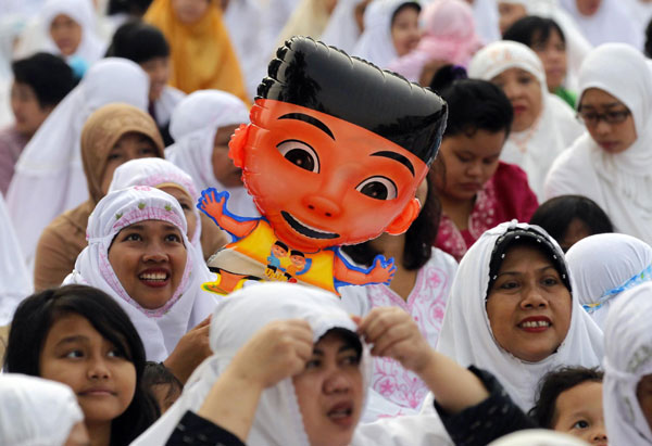 A Muslim woman holds a balloon as she attends prayer along a street to celebrate the festival of Eid al-Adha in Jakarta Nov 17, 2010. Indonesia, the world&apos;s most populous Muslim nation, celebrates Eid al-Adha by slaughtering goats and cows and distributing the meat to the poor.[China Daily/Agencies]