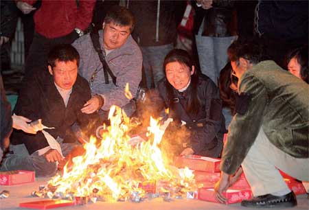Relatives of victims from Monday's high-rise building fire in Shanghai burn paper money at the site of the inferno to mourn their family members.