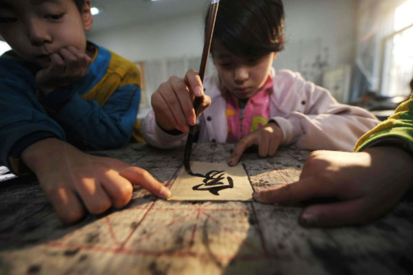 Zhang Weishi (L) watches a girl writing the Chinese character &apos;home&apos; in the SOS Children&apos;s Village in Tianjin municipality in North China on Nov 20, 2010. Zhang, 9, lives in the village which has been home for more than 300 orphans since its opening in 1984. The children here study nearby on weekdays and take part in some extracurricular classes during the weekend, including calligraphy, painting, Beijing opera and dance. [Xinhua]