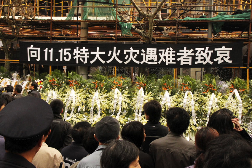 Citizens present flowers to the charred building to mourn victims of the deadly blaze in Shanghai, east China, Nov. 21, 2010. Thousands of people arrived at the site early Sunday morning to mourn at least 58 people killed in the deadly blaze of Nov. 15. Sunday is the seventh day since the disaster, a day the Chinese believe the dead would revisit their families before leaving for good. [Xinhua]