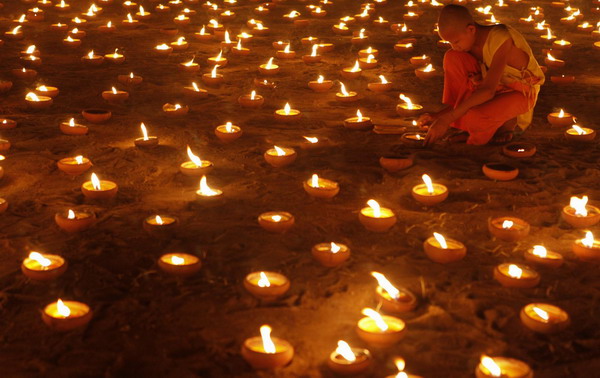 A Buddhist monk lights candles at a temple in Chiang Mai during the annual Loy Krathong festival November 21, 2010. [China Daily/Agencies]