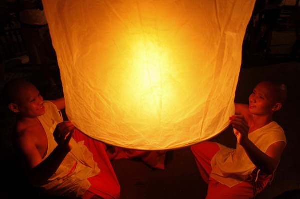 A Buddhist monk lights candles at a temple in Chiang Mai during the annual Loy Krathong festival November 21, 2010. [China Daily/Agencies]