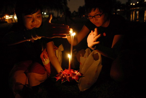 Women light a krathong, or floral float decorated with incense and candles, before releasing it into the Kallang River in Singapore as part of annual celebrations for Loy Krathong Festival November 21, 2010. [China Daily/Agencies]