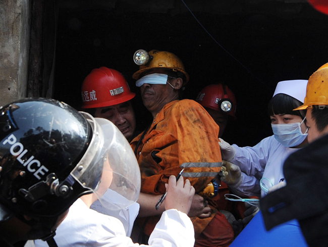 A miner, his eyes protected against the glaring light, is escorted out of the flooded mine in Weiyuan, Sichuan province, on Monday. Emergency services resuced all 29 men after they were trapped when water inundated the Batian Coal Mine at 11:40 am on Sunday. [Xinhua] 