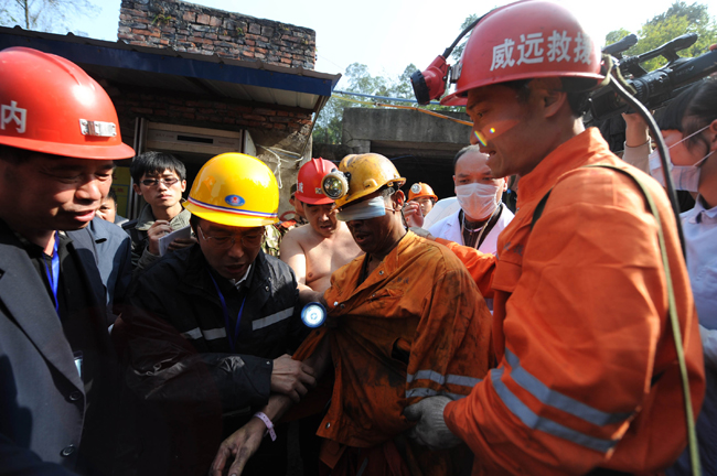 A miner, his eyes protected against the glaring light, is escorted out of the flooded mine in Weiyuan, Sichuan province, on Monday. Emergency services resuced all 29 men after they were trapped when water inundated the Batian Coal Mine at 11:40 am on Sunday. [Xinhua] 