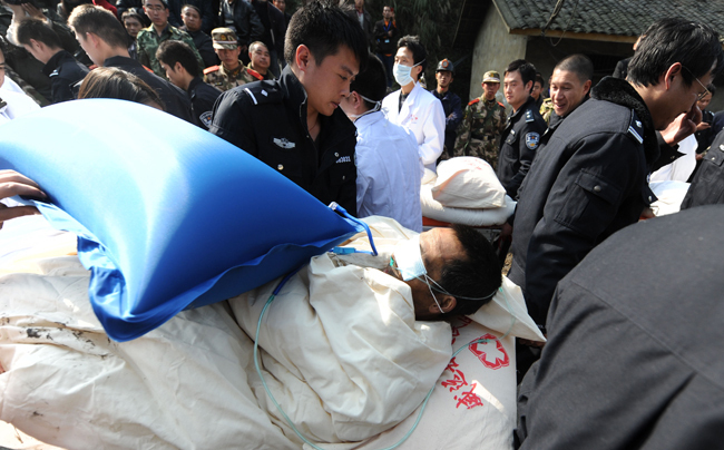 A miner, his eyes protected against the glaring light, is escorted out of the flooded mine in Weiyuan, Sichuan province, on Monday. Emergency services resuced all 29 men after they were trapped when water inundated the Batian Coal Mine at 11:40 am on Sunday. [Xinhua] 