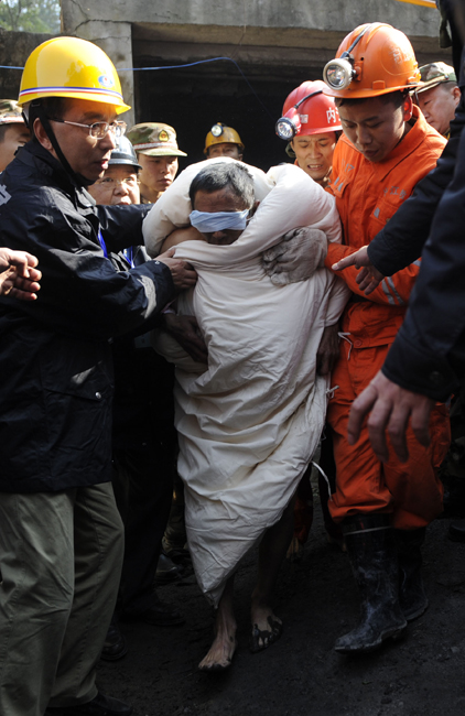 A miner, his eyes protected against the glaring light, is escorted out of the flooded mine in Weiyuan, Sichuan province, on Monday. Emergency services resuced all 29 men after they were trapped when water inundated the Batian Coal Mine at 11:40 am on Sunday. [Xinhua] 