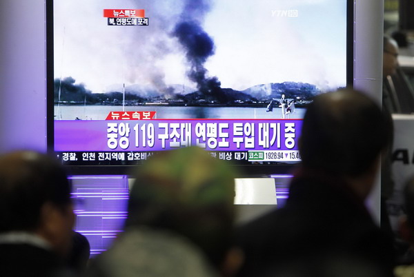 Residents in the ROK watch the news on television showing smoke rising from Yeonpyeong Island after it was hit by dozens of artillery shells fired by the DPRK, at Seoul railway station Nov 23, 2010. The DPRK on Tuesday fired dozens of artillery shells at a ROK&apos;s island, setting buildings on fire and prompting a return of fire by the ROK, Seoul&apos;s military and media reports said. The Korean characters on the screen read, &apos;North Korea fired on Yeonpyeong Island&apos;. [China Daily/Agencie]