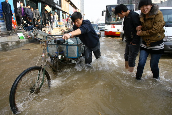 Pedestrians cross a street flooded by a burst tap water pipe in Zhengzhou, Henan province, on Monday afternoon. The previous incident of a burst pipe in the city occurred just five days ago and led to the water supply to 800,000 residents being cut off.