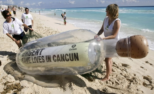Activists of Oxfam, an international charity, carry a giant bottle, containing a message that reads, 'Urgent: Save Lives in Cancun,' in reference to millions of the world's poorest people, on the shores of a beach in Cancun, Mexico, on Sunday. [Photo/Agencies]