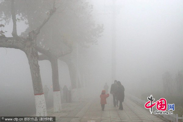 Pepople walk across a road in dense fog in Xingtai, North China&apos;s Hebei province on the morning of Dec 1, 2010. Heavy fog shrouded China&apos;s central and eastern regions Wednesday morning, causing road closures in some areas. [CFP]