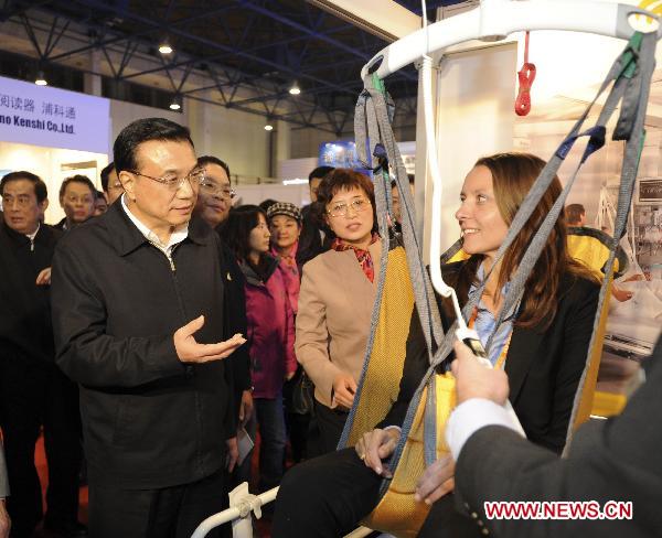 Chinese Vice Premier Li Keqiang (L, front) looks at a mobility assisting device for the disabled during his visit to the Care and Rehabilitation Expo China 2010 in Beijing, capital of China, Dec. 3, 2010. Friday marked the International Day for Persons with Disabilities. (Xinhua/Xie Huanchi)