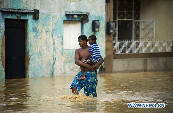 A man carries his son to cross a flooded road in Higuerote, Miranda, Venezuela. Dec. 5, 2010. [Xinhua]