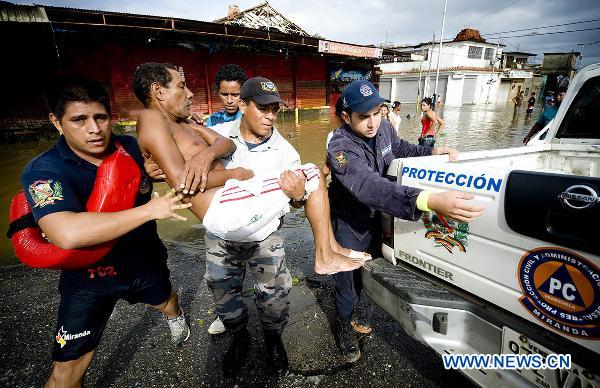 Members of Miranda State Civil Protection and rescue volunteers help to carry a man to a vehicle on a flooded road in Higuerote, Miranda, Venezuela. Dec. 5, 2010. [Xinhua]