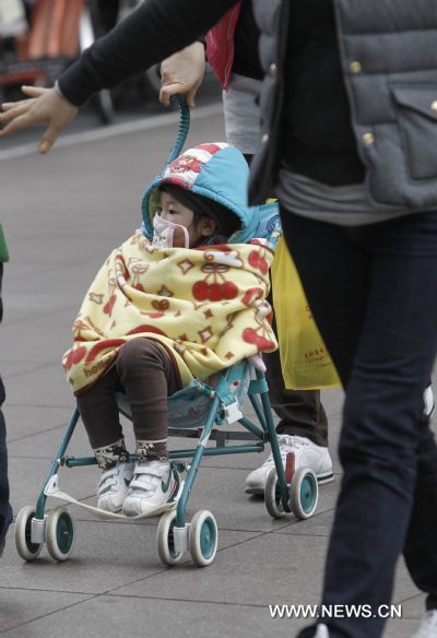 A child covered with thick clothes sits in a baby cart in a street in Shanghai, east China, Dec. 6, 2010. Many places in China witnessed strong wind and significant temperature drop due to a cold wave.[Xinhua]