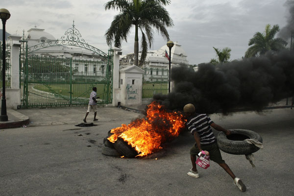 A Haitian sets up a barricade made with burning tyres while holding a banner of presidential candidate Michel Martelly in front of the national palace in Port-au-Prince December 8, 2010.[Xinhua]