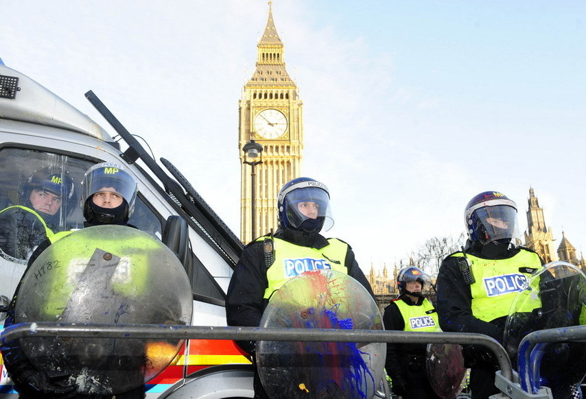 Policemen whose shields were spilled with paint thrown by protesters stand guard in front of the Parliament Building in London, Britain, Dec. 9, 2010. [Xinhua]