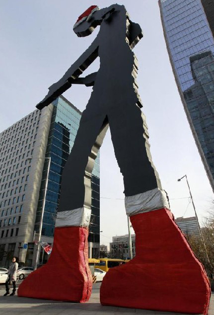 A pedestrian walks by the 22-metre-high, 50-tonne statue titled &apos;Hammering Man&apos; by US artist Jonathan Borofsky, in Seoul Dec 7, 2010. [China Daily/Agencies] 