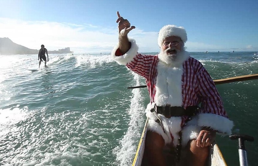 Donald Boyce, dressed as Santa Claus, does a &apos;shaka&apos; as he shares a wave with a surfer while riding in an outrigger canoe off Waikiki beach in Honolulu, Hawaii in this still image taken from video Dec 11, 2010.[China Daily/Agencies] 