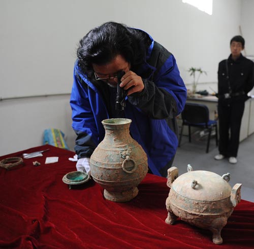 Using a flashlight, archaeologist Liu Daiyun checks the liquid in a bronze pot unearthed in an ancient tomb in Xi'an, capital of Northwest China's Shaanxi province, Dec 10, 2010. [Photo/Xinhua] 