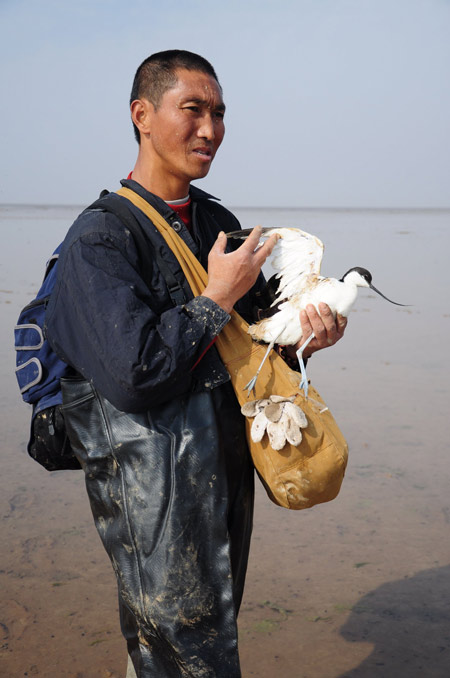 Huang Xianyin holds an injured snipe at Poyang Lake on Friday. The injured bird was abandoned bird after it got caught in a net. 